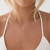 Close-up of a person wearing a gold necklace with heart pendants on a plain background