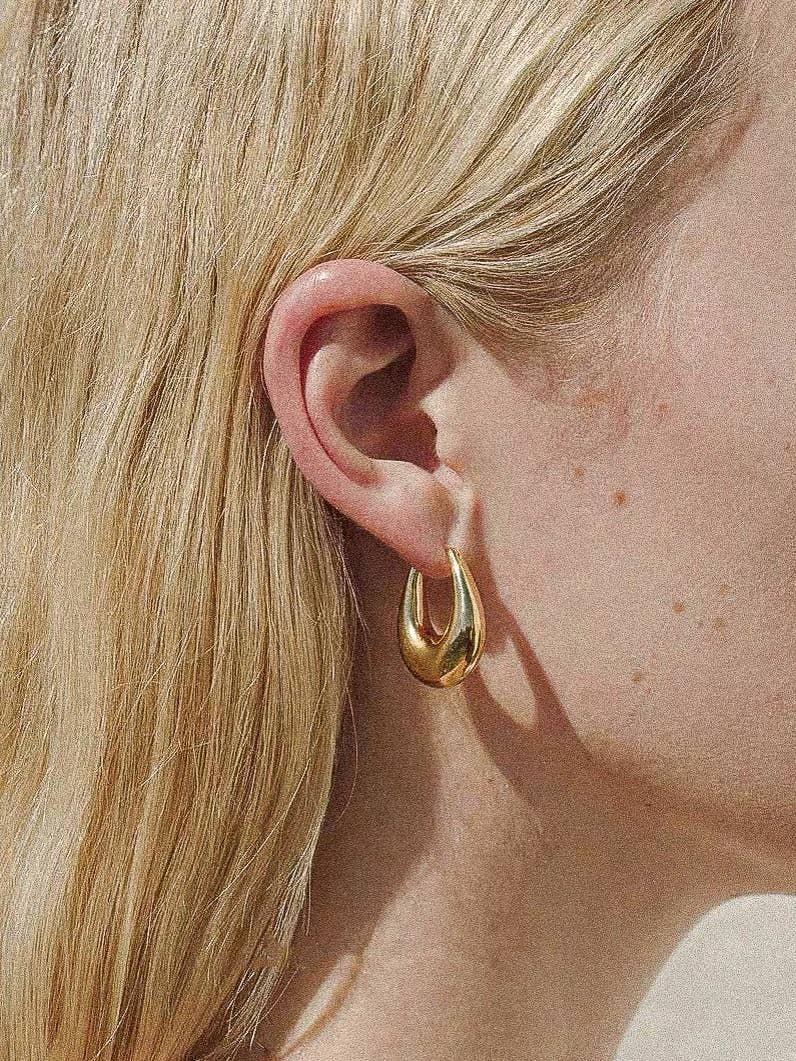 Gold droplet hoop earrings with a gently curved silhouette and smooth, polished finish. Crafted from 18K gold-plated brass, measuring 1 x 0.7 inches. Hypoallergenic, water- and tarnish-resistant—ideal for effortless everyday elegance.