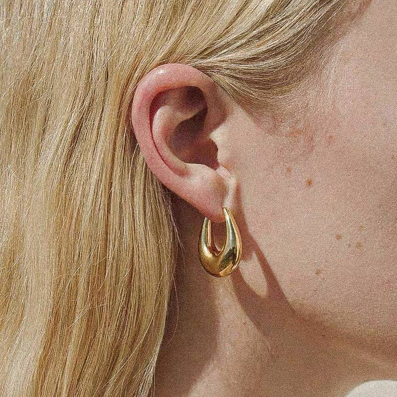 Gold droplet hoop earrings with a gently curved silhouette and smooth, polished finish. Crafted from 18K gold-plated brass, measuring 1 x 0.7 inches. Hypoallergenic, water- and tarnish-resistant—ideal for effortless everyday elegance.