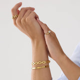 Close-up of a person wearing gold bracelets and rings on a light background