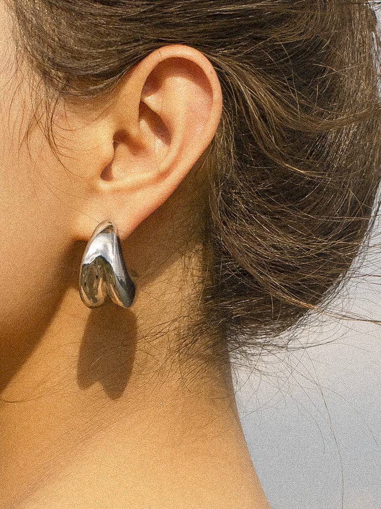 Remi Double Huggie Earring in 18K gold plated stainless steel, featuring a sleek double-band design that creates a stacked hoop look, styled by a model. 