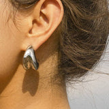 Remi Double Huggie Earring in 18K gold plated stainless steel, featuring a sleek double-band design that creates a stacked hoop look, styled by a model. 