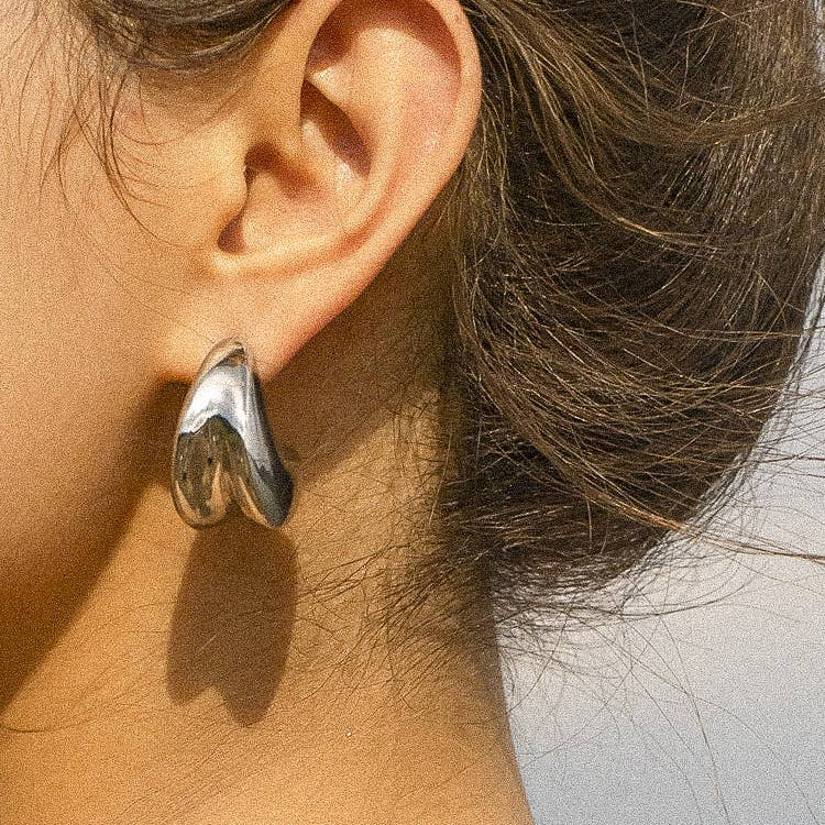 Remi Double Huggie Earring in 18K gold plated stainless steel, featuring a sleek double-band design that creates a stacked hoop look, styled by a model. 