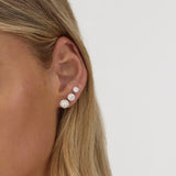 Close-up of an ear wearing a diamond earring on a plain background
