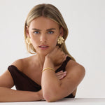 Woman wearing gold earrings and bracelet on a white background