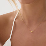 Gold necklace with a heart pendant worn by a person against a neutral background