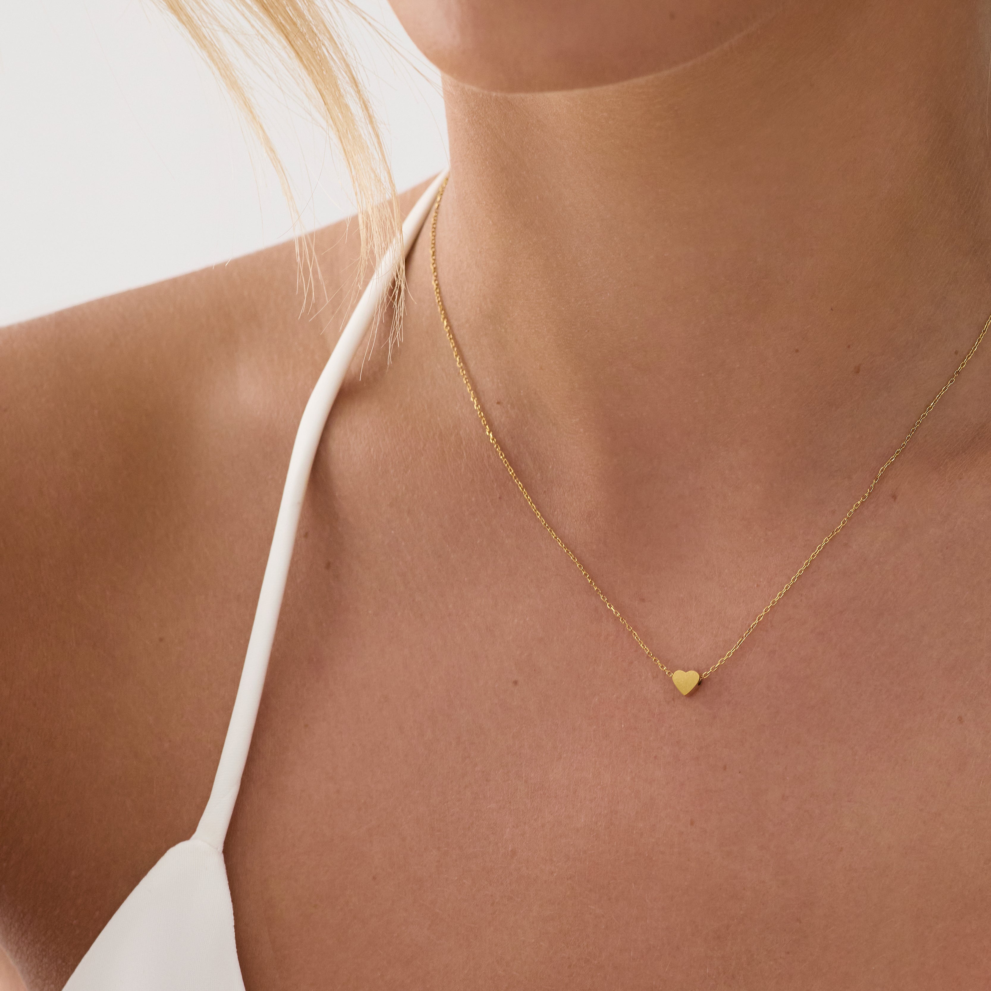 Gold necklace with a heart pendant worn by a person against a neutral background