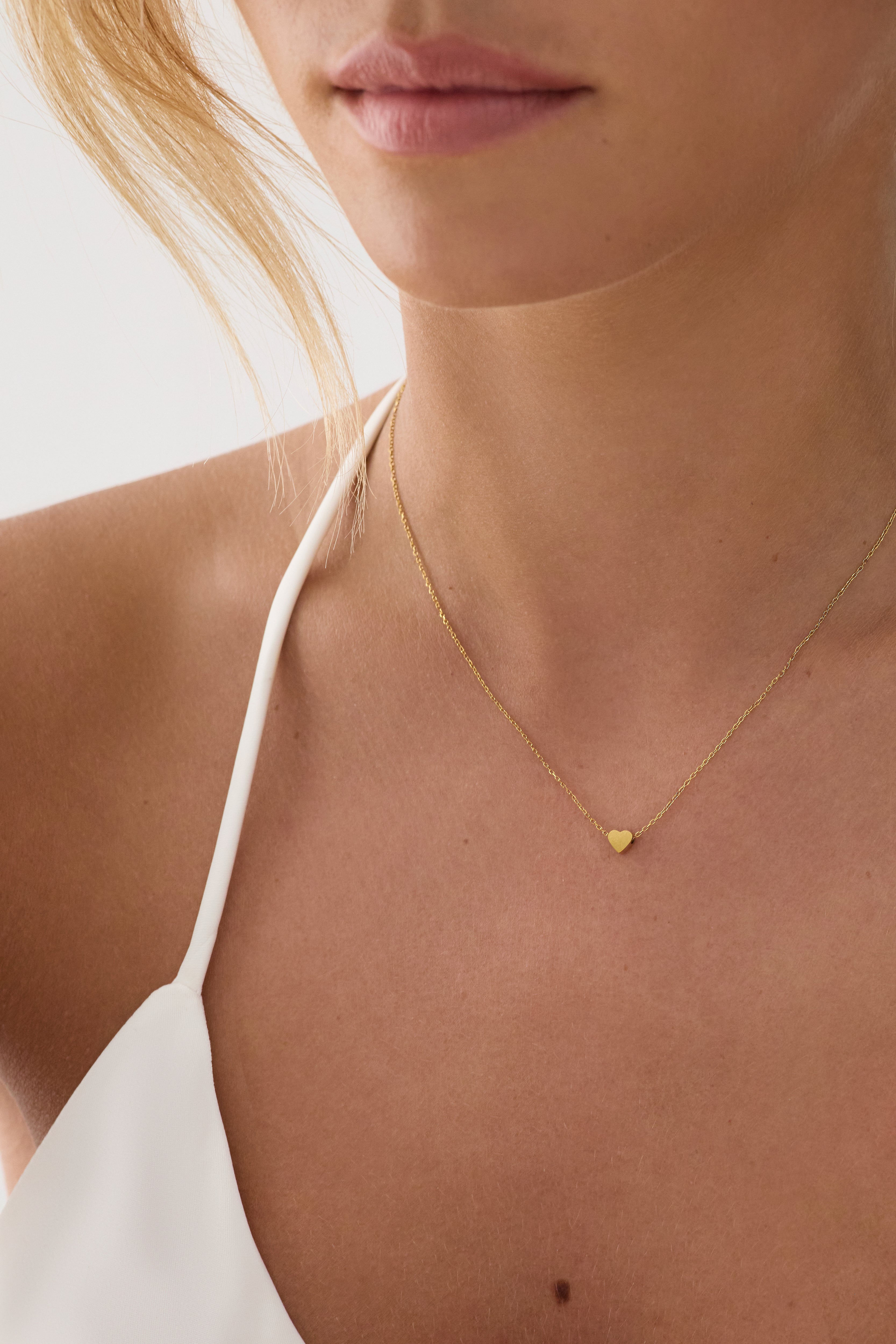 Gold necklace with a heart pendant worn by a person against a neutral background