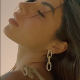 Close-up of a person wearing a chain-link earring with a neutral background