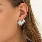 Silver heart-shaped stud earrings on model. 