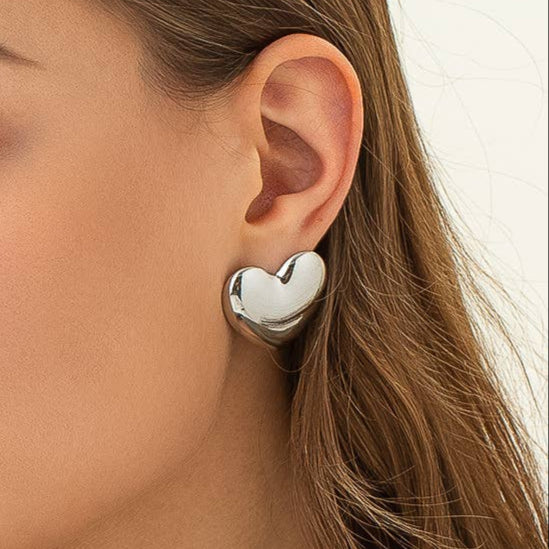 Silver heart-shaped stud earrings on model. 